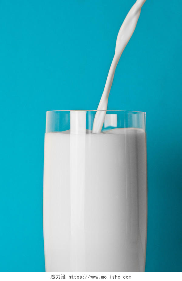 蓝底牛奶到入玻璃杯中背景图片